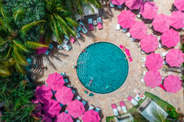 Circular hotel pool surrounded by pink umbrellas