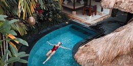 woman floating in tropical hotel pool by cabana